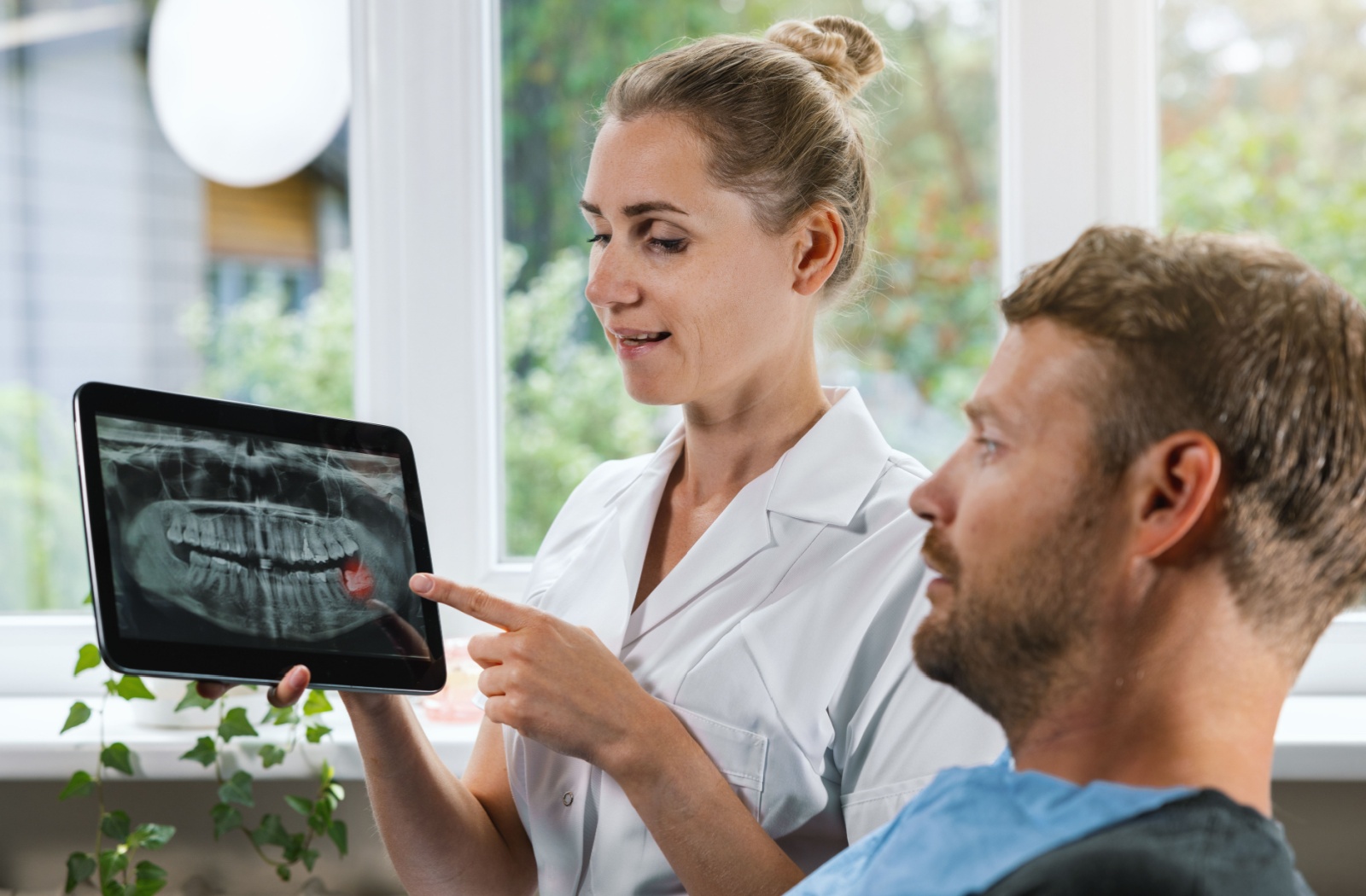 A dentist shows a patient on a handheld tablet an x-ray of their teeth showcasing the wisdom teeth that are impacted