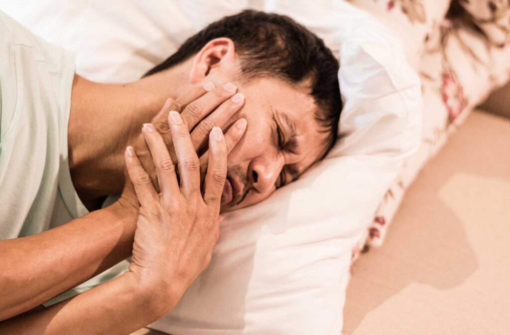 An adult holds their jaw, clearly in pain, as they lay in their bed.