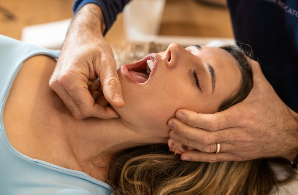 A healthcare professional massages an adults jaw to help improve its function.