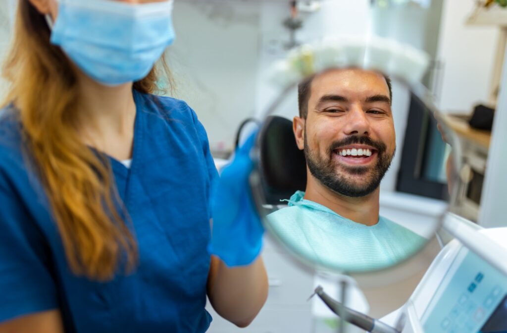 A dental patient smiling in a handheld mirror at the dentist after receiving treatment for periodontal disease.