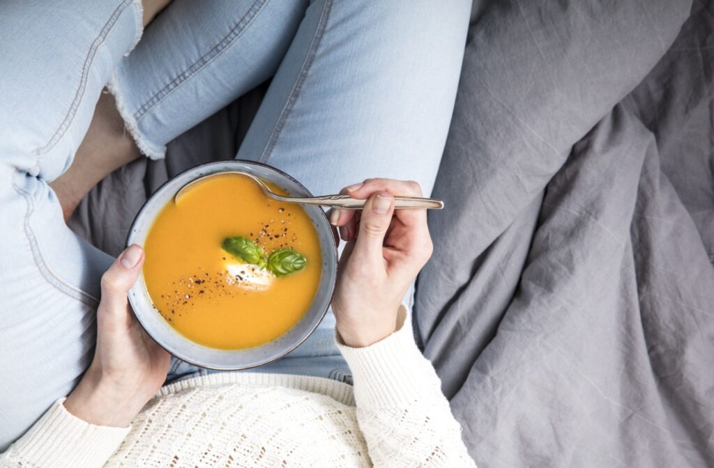 A bowl of soup sitting on a person's lap, who is eating it due to temporary Invisalign soreness.